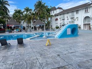 Une piscine dotée de chaises longues, d’un toboggan et d’un bâtiment comportant plusieurs balcons.