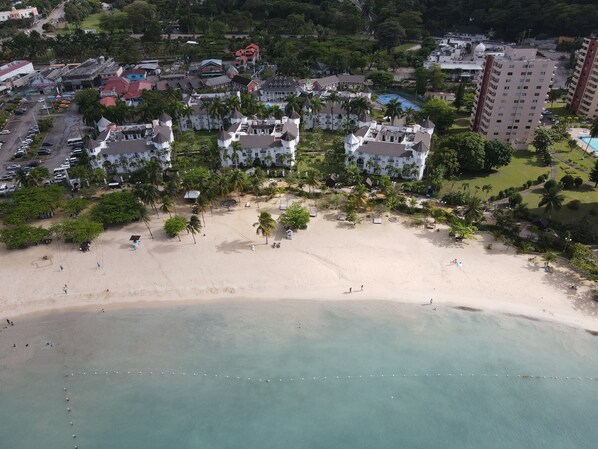 An aerial view of a coastal resort with beachfront villas, a sandy beach, and a clear blue sea.