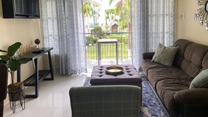 A living room with a sofa, a coffee table, a TV, and a balcony with patterned curtains. - Ocho Rios Sandcastles King Suite with Balcony & Beach Access – Ideal for Couples (Ocho Rios)