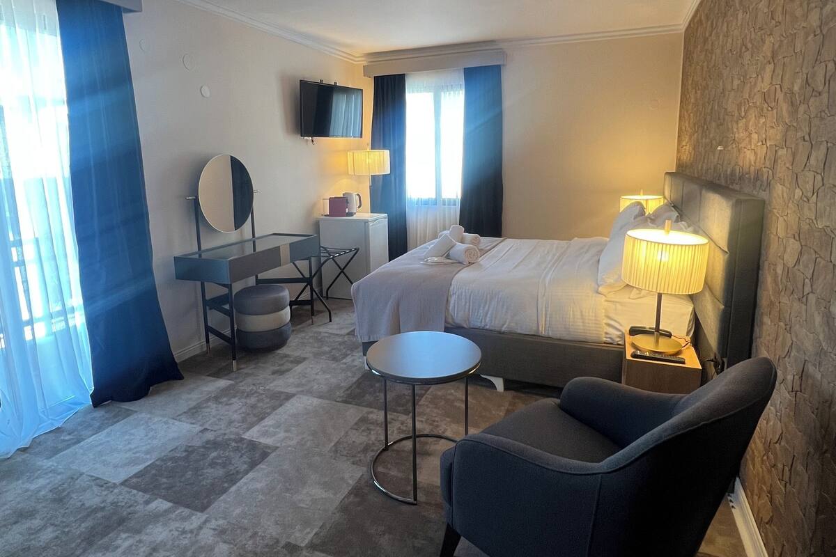 A hotel room with a bed, a desk with a chair, a small round table, a sofa, and a TV on the wall.