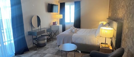 Habitación de hotel con cama, escritorio con silla, una mesita redonda, sofá y televisor en la pared.