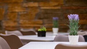 Un comedor con una mesa blanca y sillas marrones. Hay una planta en maceta con flores moradas sobre la mesa.
