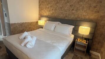 Una cama bien hecha con sábanas y toallas blancas, dos lámparas de noche, una pared de acento de piedra y una mesita.