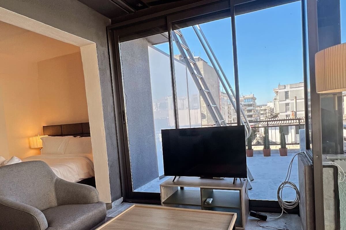 A modern hotel room with a large window, a flat-screen TV, a sofa, and a coffee table.