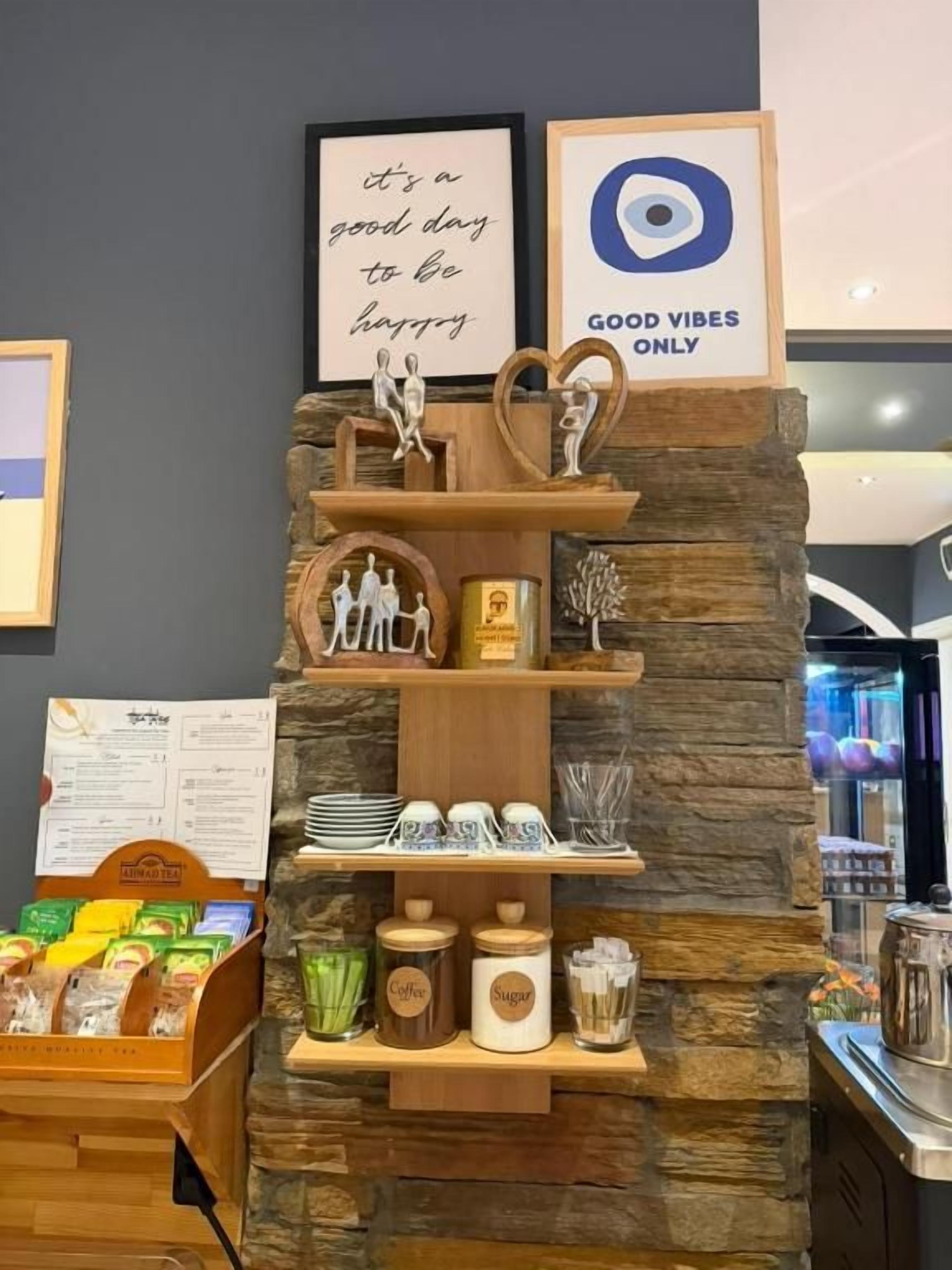 A coffee station with a stone wall backdrop, featuring a sign that says 'it's a good day to be happy' and another that reads 'GOOD VIBES ONLY'.