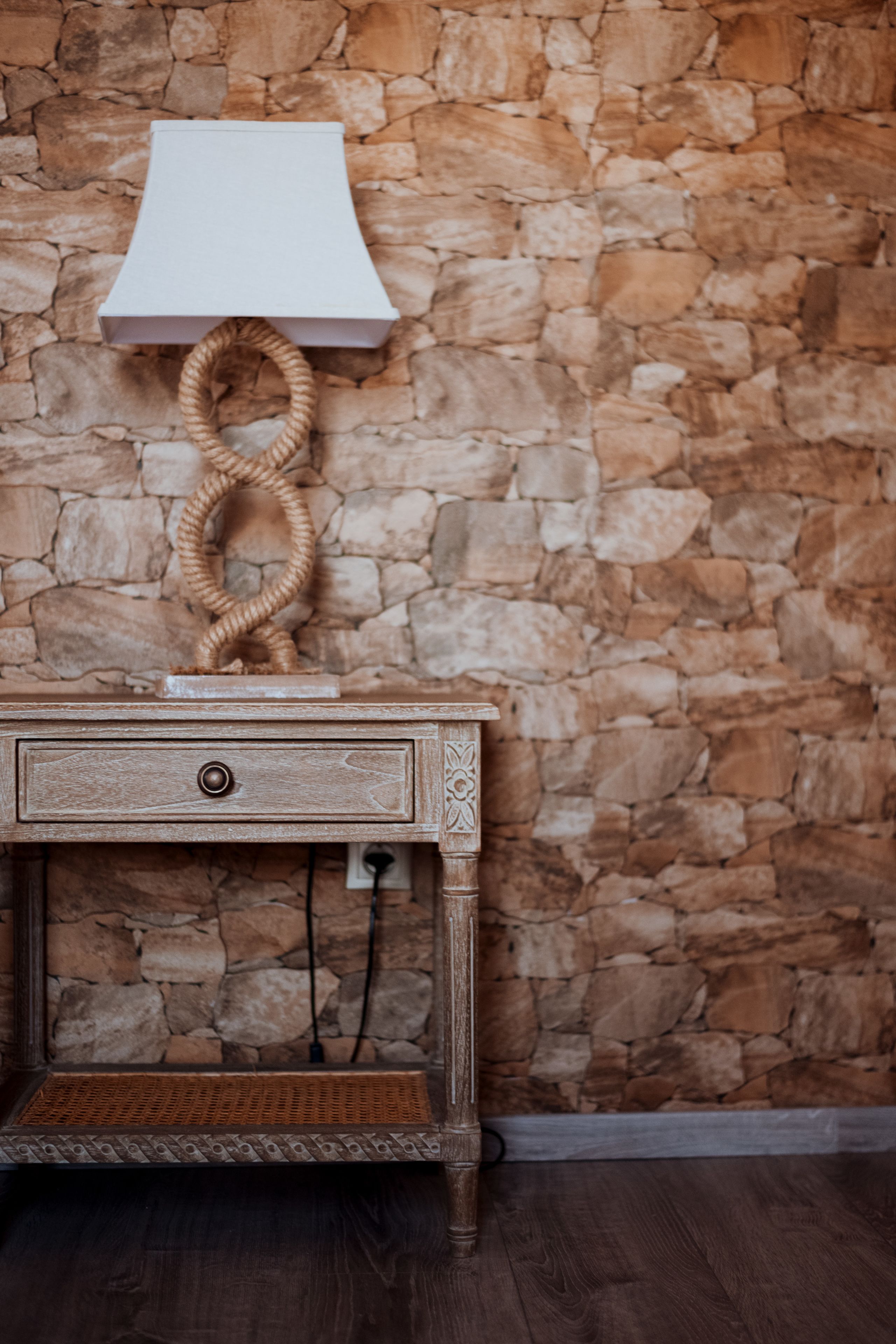 Een houten nachtkastje met een lamp, een lade en een decoratieve touw.
