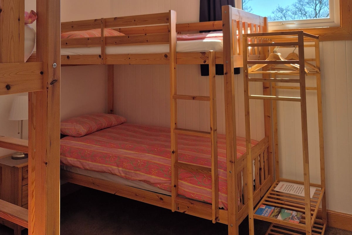 A bunk bed room with a window, a hanging light fixture, and a wooden ladder.