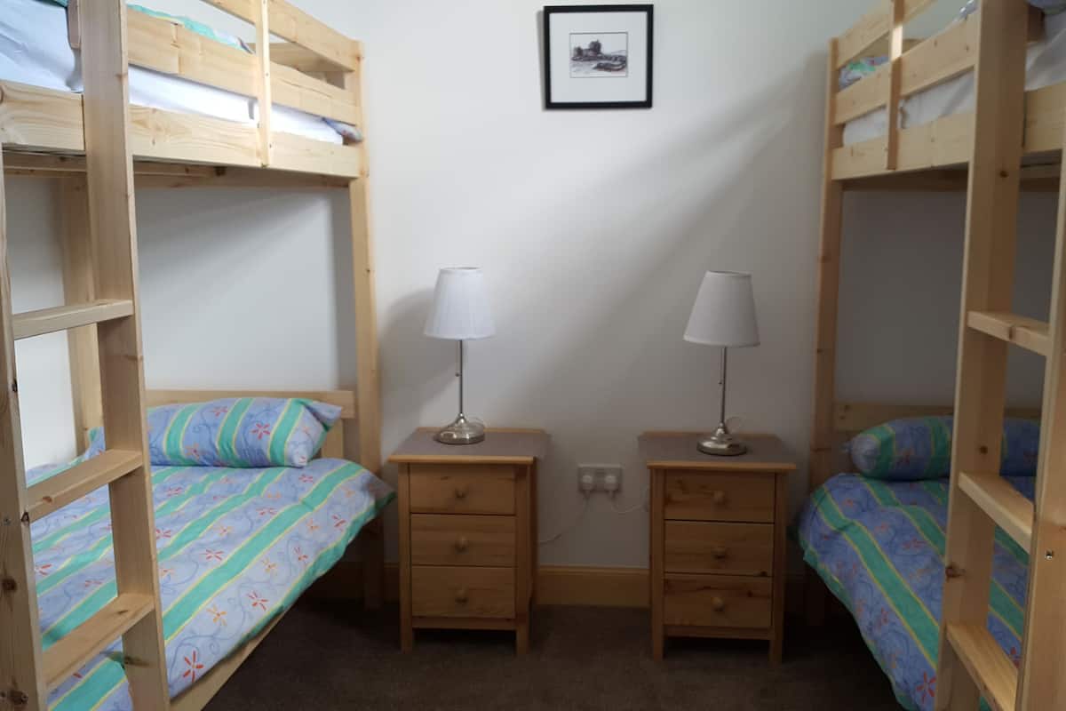 A dormitory room with bunk beds, two bedside tables with lamps, and a framed picture on the wall.