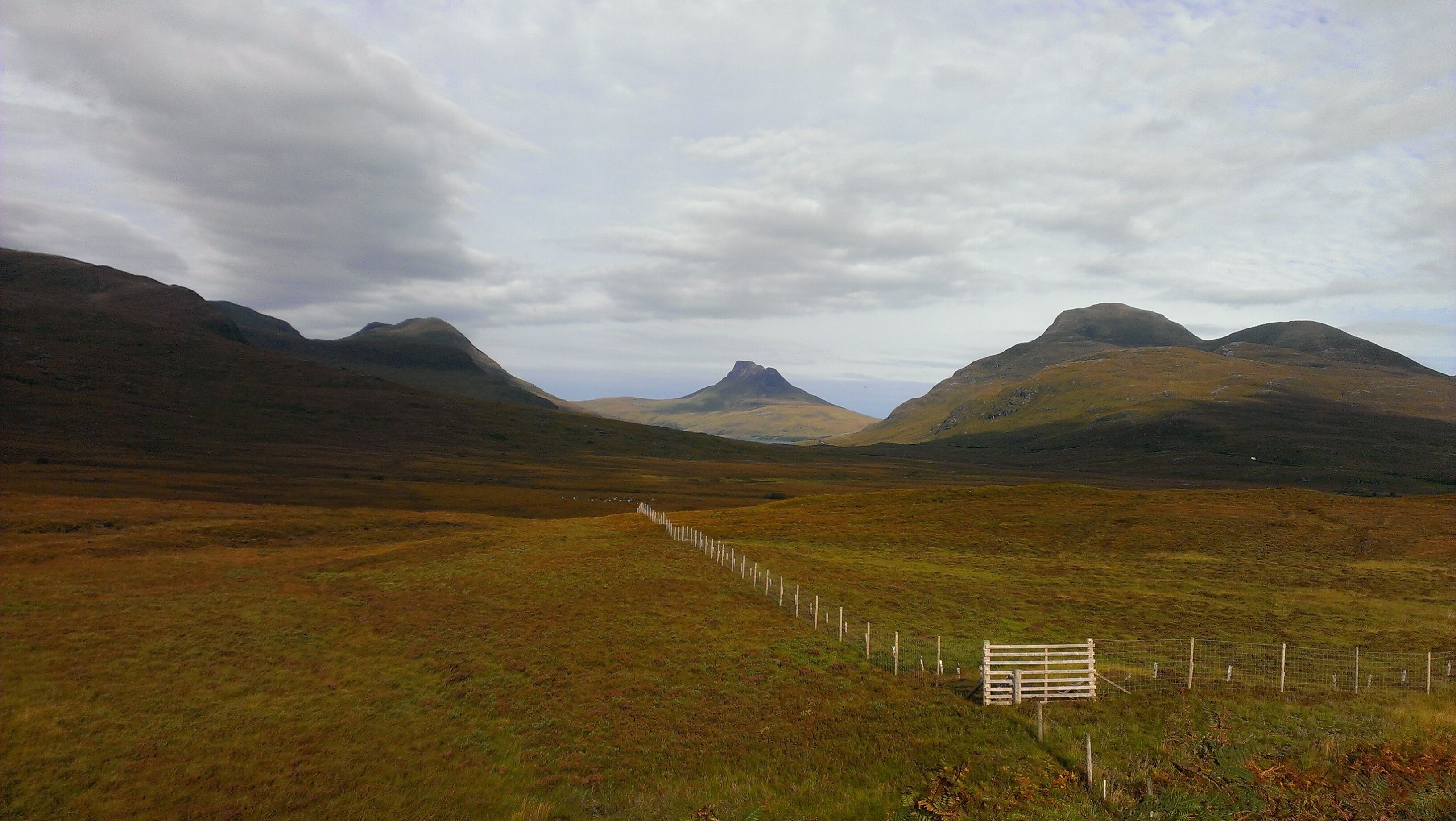 A rural landscape with mountains, a fenced field, and a signpost.