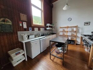 A kitchen with wooden floors, a window, a sink, a refrigerator, a stove, and a shelf with dishes. - Helmsdale Lodge (Helmsdale)