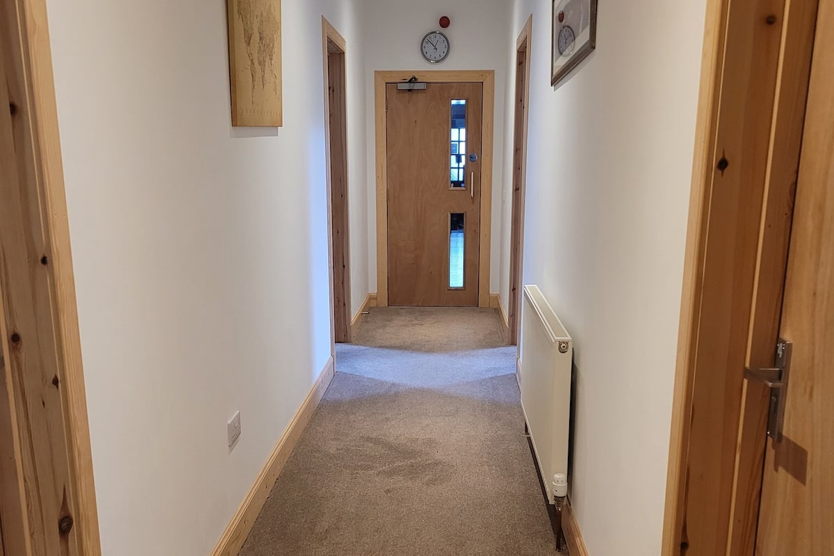 A narrow hallway with wooden doors, a carpeted floor, and a clock on the wall.