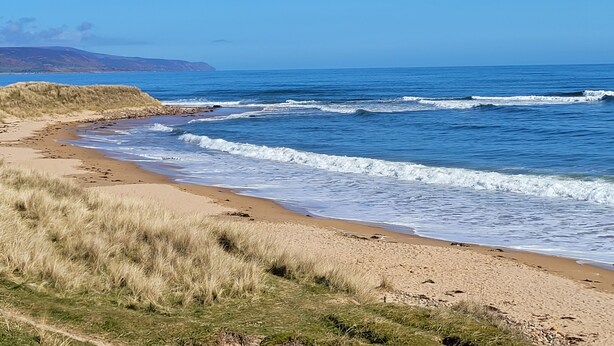 A beach with waves, a clear sky, and distant hills. - Helmsdale Lodge (Helmsdale)