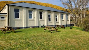 A building with a flat roof, multiple windows, and a grassy lawn with picnic tables. - Helmsdale Lodge (Helmsdale)