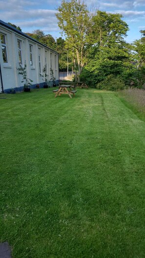 A well-maintained grassy lawn with picnic tables, a white building with multiple windows, and trees in the background. - Helmsdale Lodge (Helmsdale)
