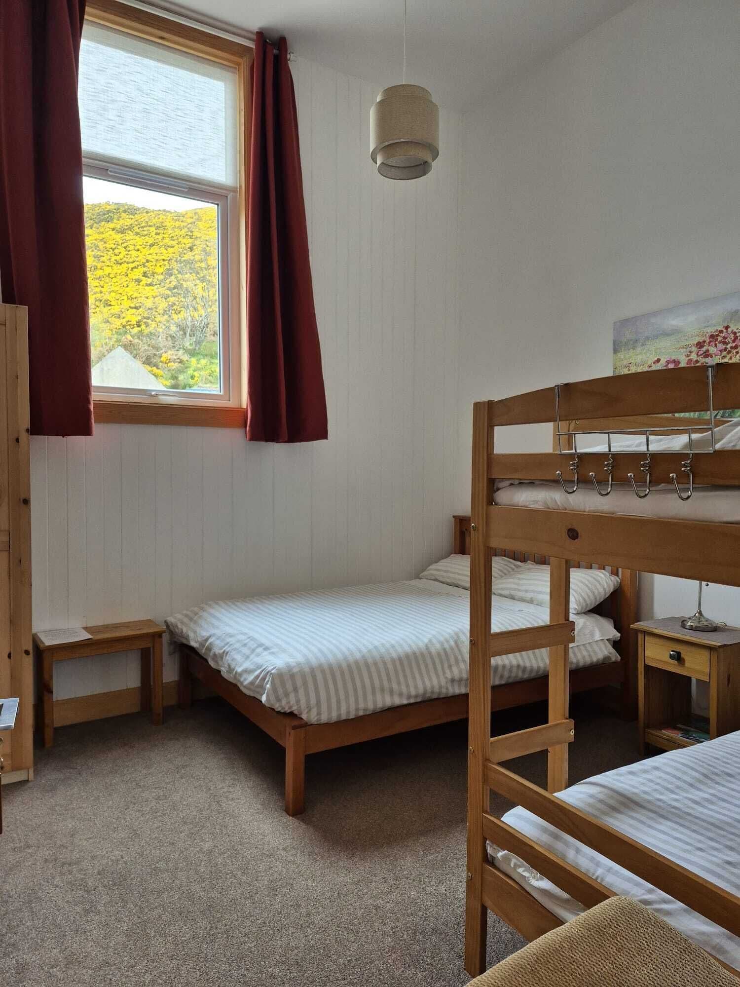 Una habitación con dos literas, una mesita de noche con lámpara, una ventana con cortinas y un cuadro en la pared.