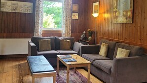A cozy living room with wooden walls, a sofa, a coffee table, and a window with curtains. - Helmsdale Lodge (Helmsdale)