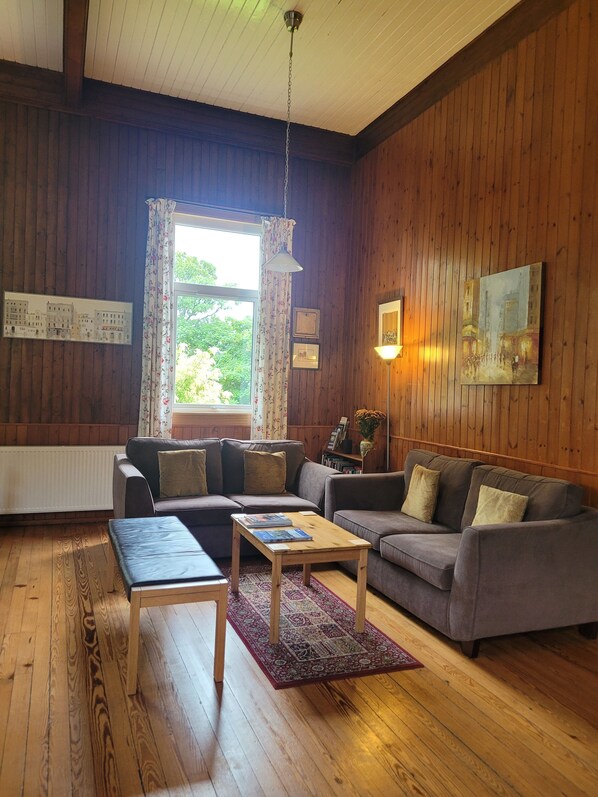 A cozy living room with wooden walls, a sofa, a coffee table, and a window with curtains.