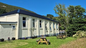 A building with a flat roof, multiple windows, and a grassy lawn with picnic tables. - Helmsdale Lodge (Helmsdale)