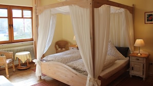 Un lit à baldaquin avec des rideaux blancs, une table de chevet en bois avec une lampe, une chaise en osier et une petite table avec une lampe.
