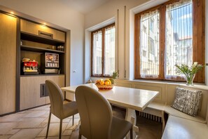 A modern kitchen with a built-in espresso machine, a dining table with chairs, and a window seat with a plant. - Blu Notte Guest House (Florence)