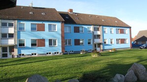 A multi-story residential building with a flat roof, multiple windows, and a well-maintained lawn with rocks. - Haus Marinus (Fehmarn)
