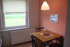A room with a window, a table with chairs, a radiator, and a wall-mounted lamp.