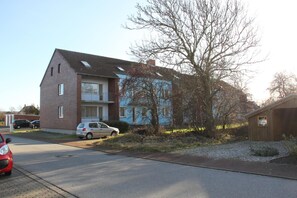 A two-story residential building with a garage, a parked car, and a tree in front.