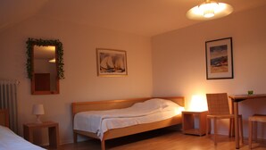 A hotel room with a wooden bed, a desk with a chair, a lamp, and two paintings on the wall. - Haus Marinus (Fehmarn)