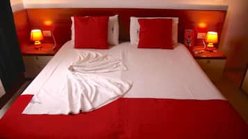 A hotel room with a large bed, red and white bedding, two bedside lamps, and a red throw blanket.