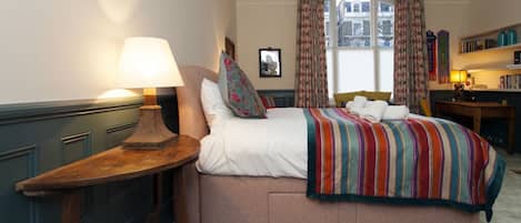 A bedroom with a bed, a nightstand, a lamp, a window with curtains, a bookshelf, and a floral rug.