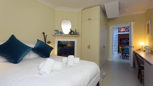 A hotel room with a bed, pillows, a mirror, a fireplace, a desk, and a chair.