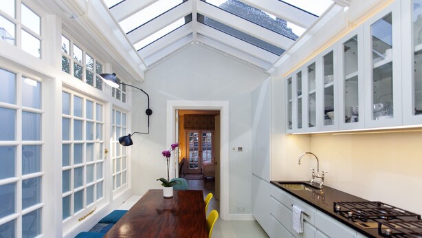 A kitchen with a wooden dining table, white cabinets, and a skylight.