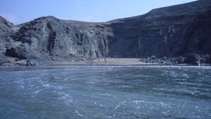 Une plage de galets offrant une vue dégagée sur l’eau, où l’on aperçoit une personne debout sur le sable.