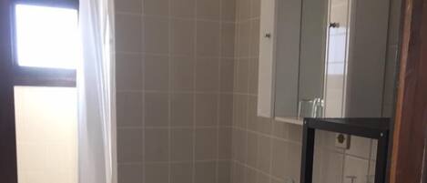 A small, clean bathroom with a toilet, sink, and mirror. There is a shower curtain and a shelf with toiletries.