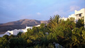 Un paysage côtier avec des bâtiments blancs, des palmiers et une montagne en arrière-plan.