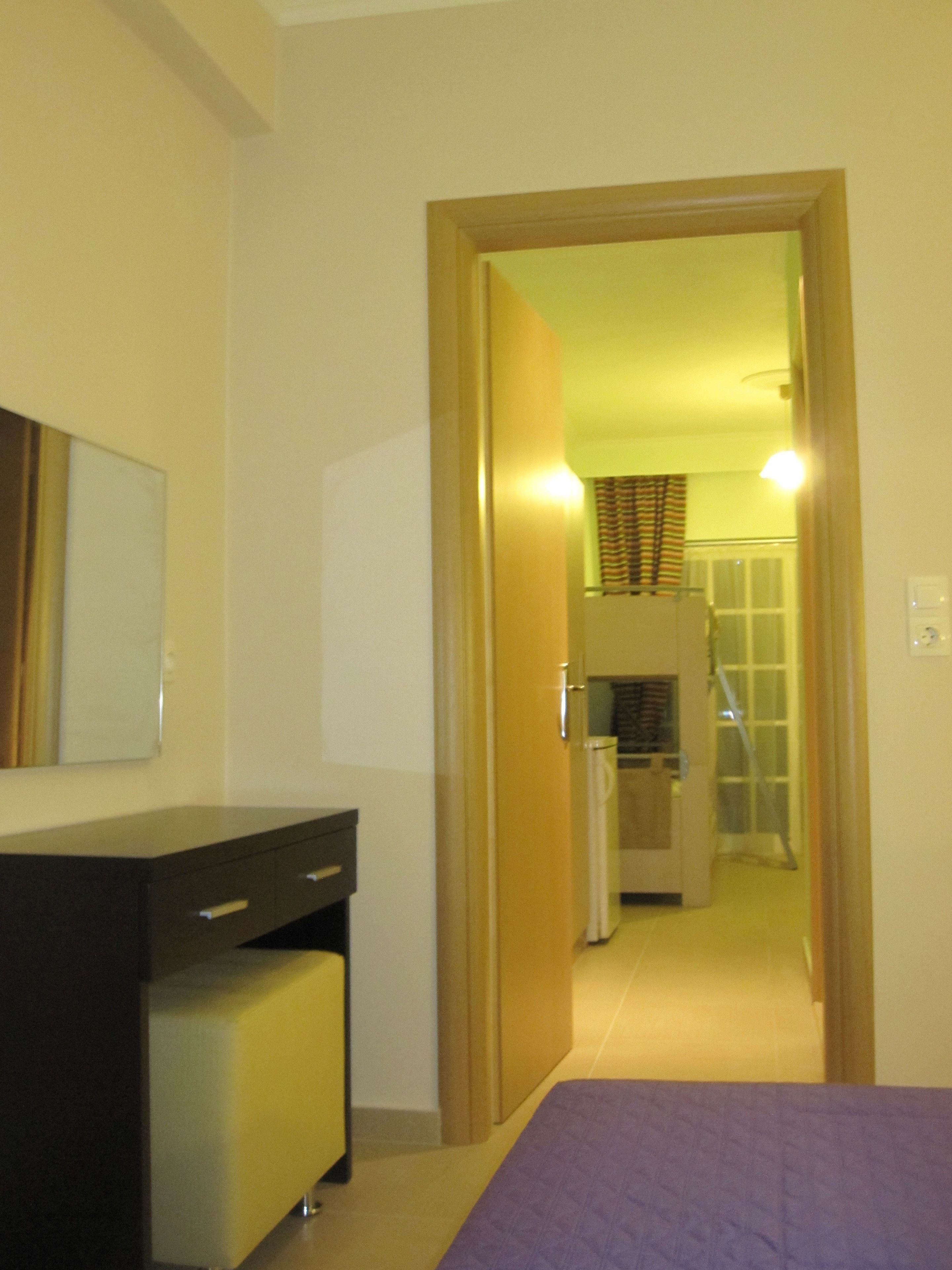 Una habitación de hotel con cama, escritorio y armario. Hay un pasillo que conduce a un baño y una zona de cocina.