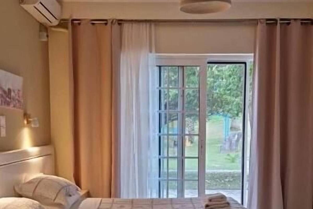 A bedroom with a large bed, a ceiling fan, and a view of a garden through a sliding glass door.