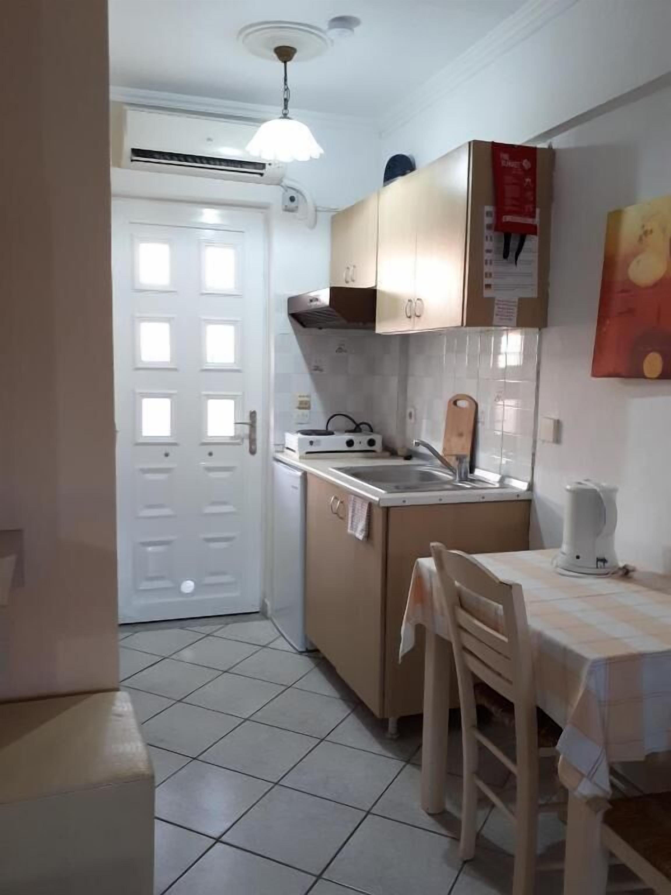 A compact kitchen with a white door, a small dining table with chairs, and a tiled floor.