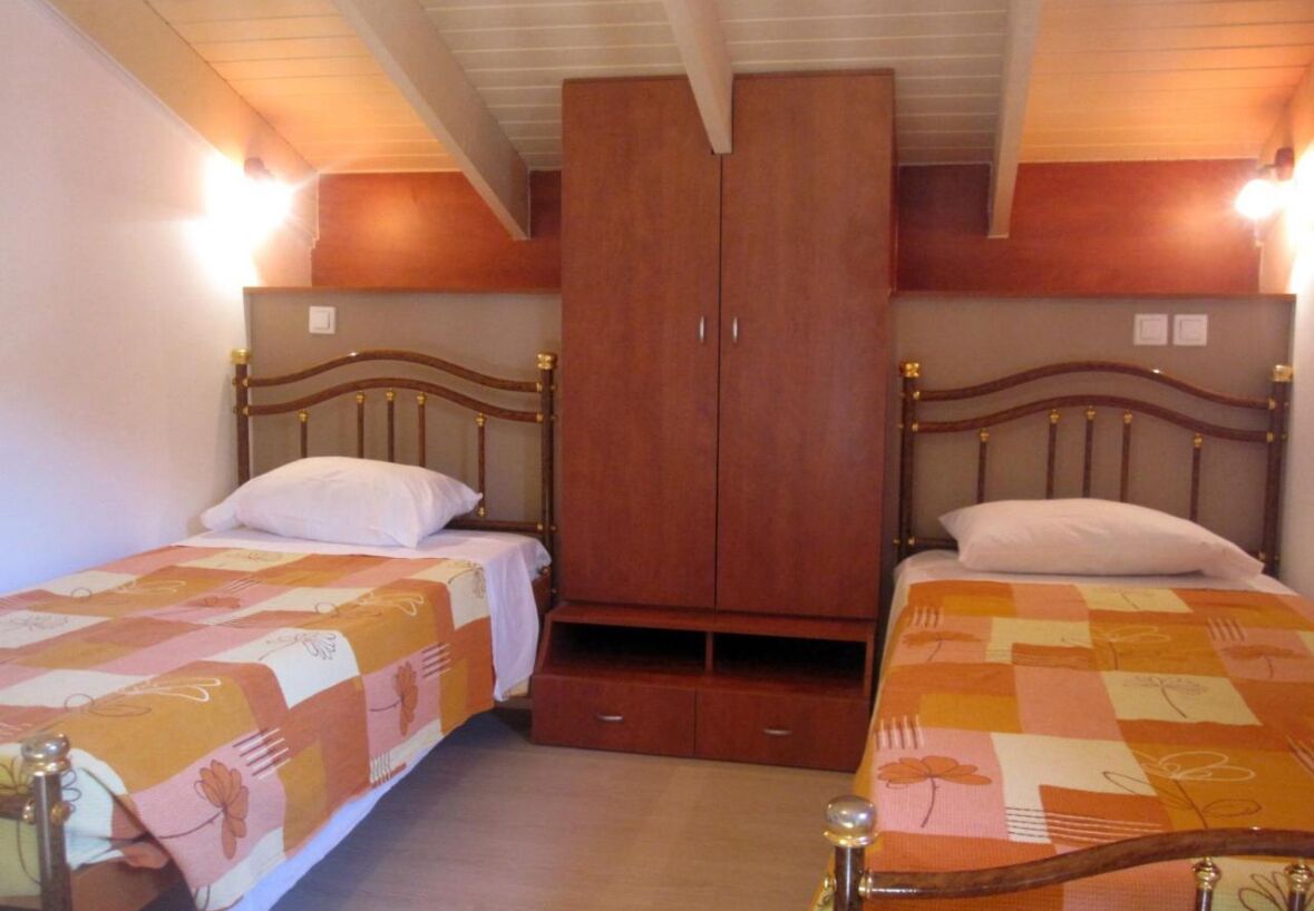 A bedroom with two single beds, a wooden wardrobe, and a small shelf unit.