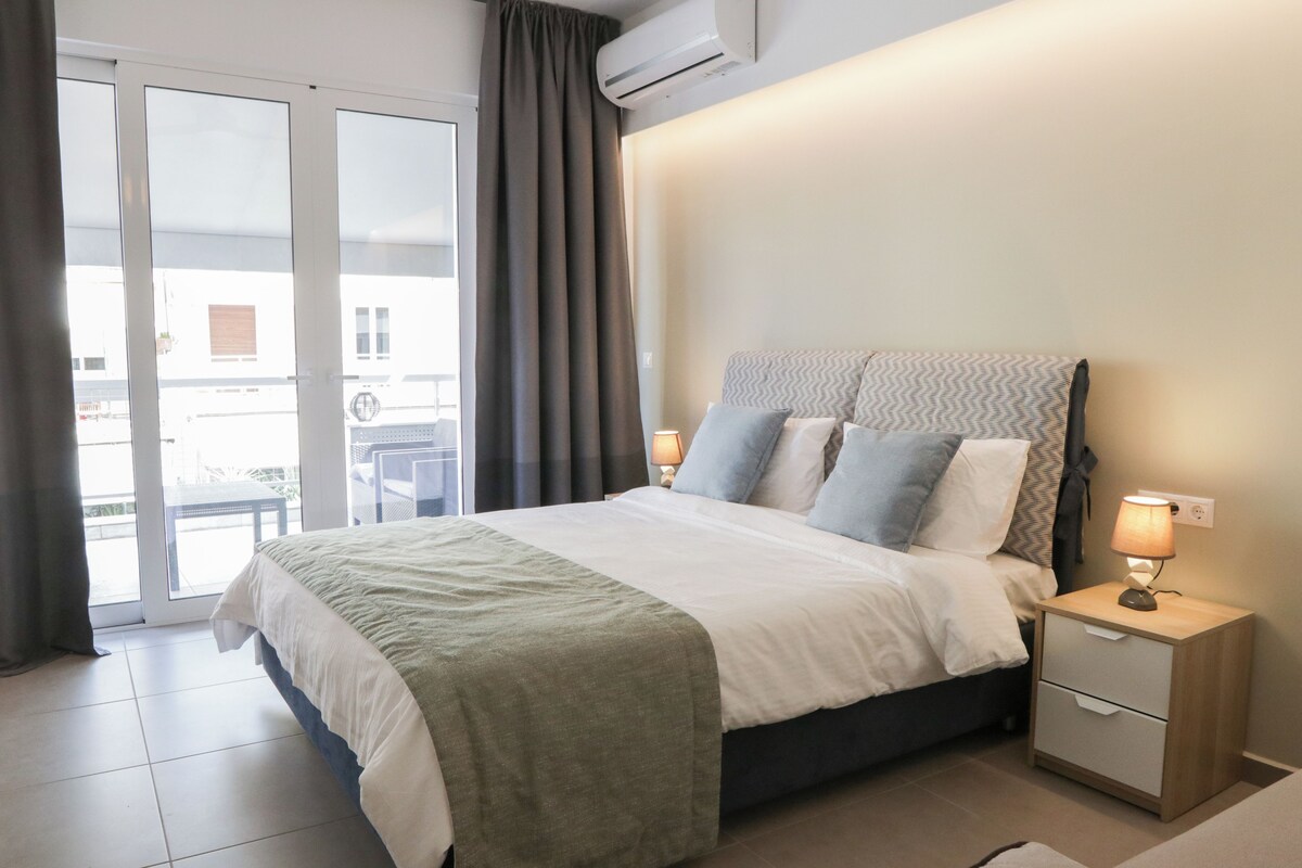 A hotel room with a bed, bedside tables, and a view through a sliding door to an outdoor area.