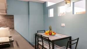 Cocina compacta con comedor, que incluye una mesa de madera con frutero, hervidor y tostadora.