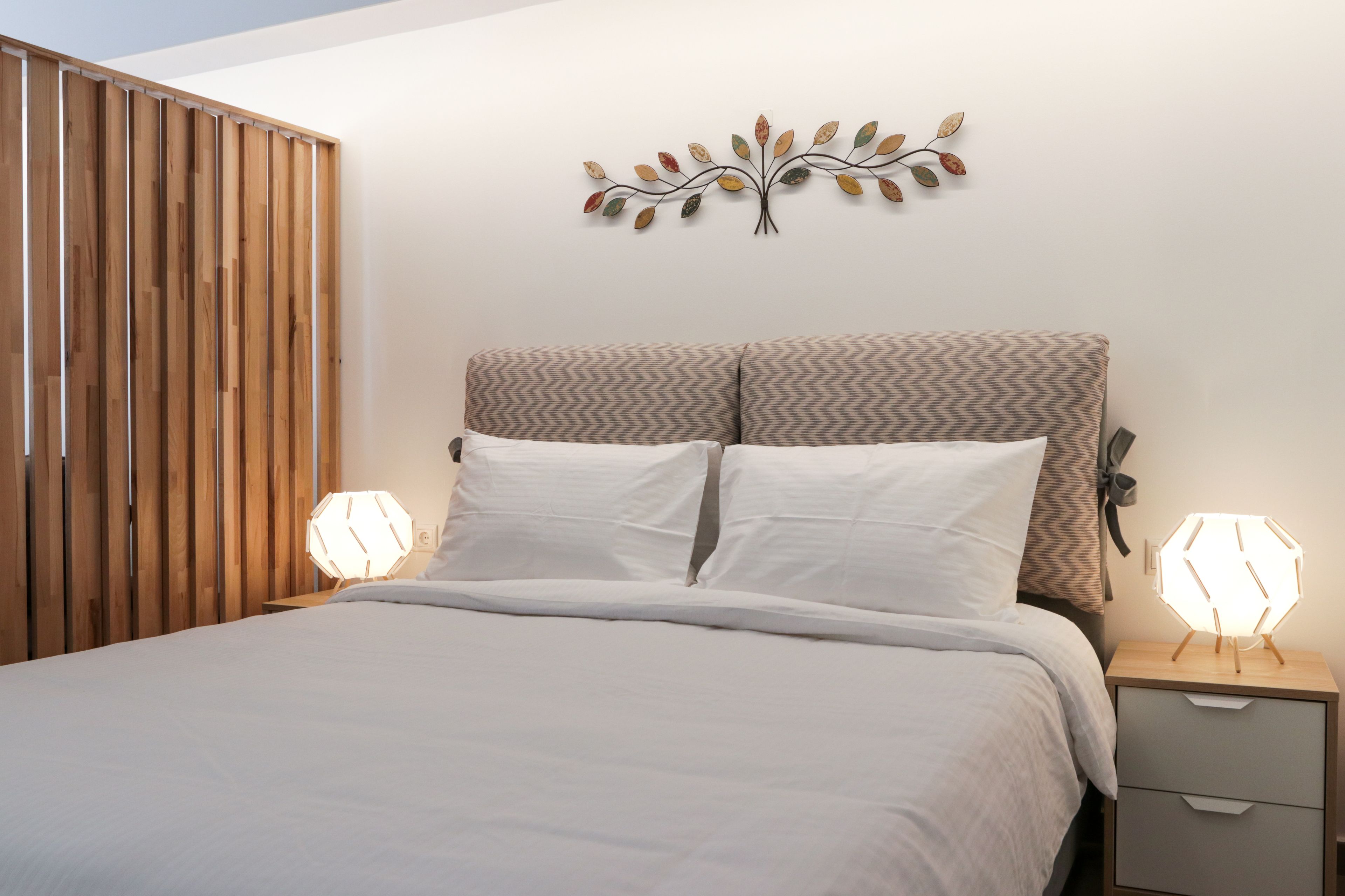 A bedroom with a bed, two bedside tables, a wall-mounted light fixture, and a wooden partition.