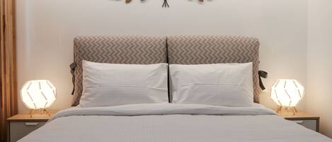 A neatly made bed with a headboard, two bedside lamps, and a wall-mounted decorative piece.