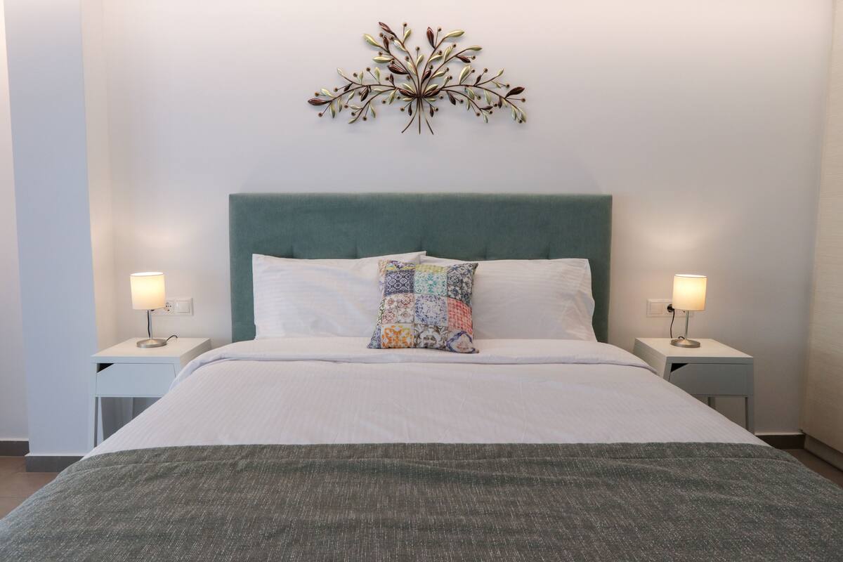 Una cama bien tendida con un cabecero verde, dos mesitas de noche con lámparas y un adorno decorativo sobre la cama.