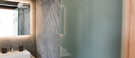 A bathroom with a marble wall, a sink with a mirror, and a glass shower door.