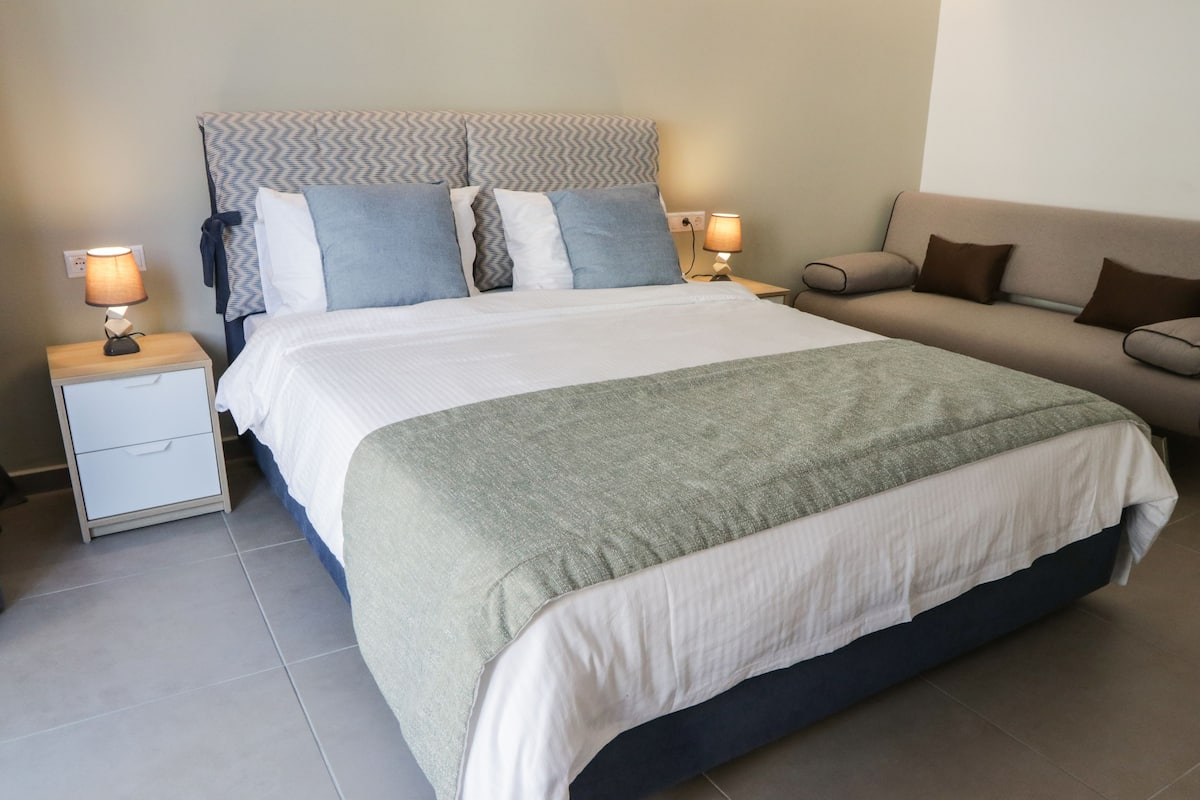 Una habitación de hotel ordenada con una cama, un sofá y dos mesitas de noche con lámparas.