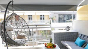 Un balcón con una hamaca colgante, una mesita con fruta, un sofá con cojines y vistas a edificios.