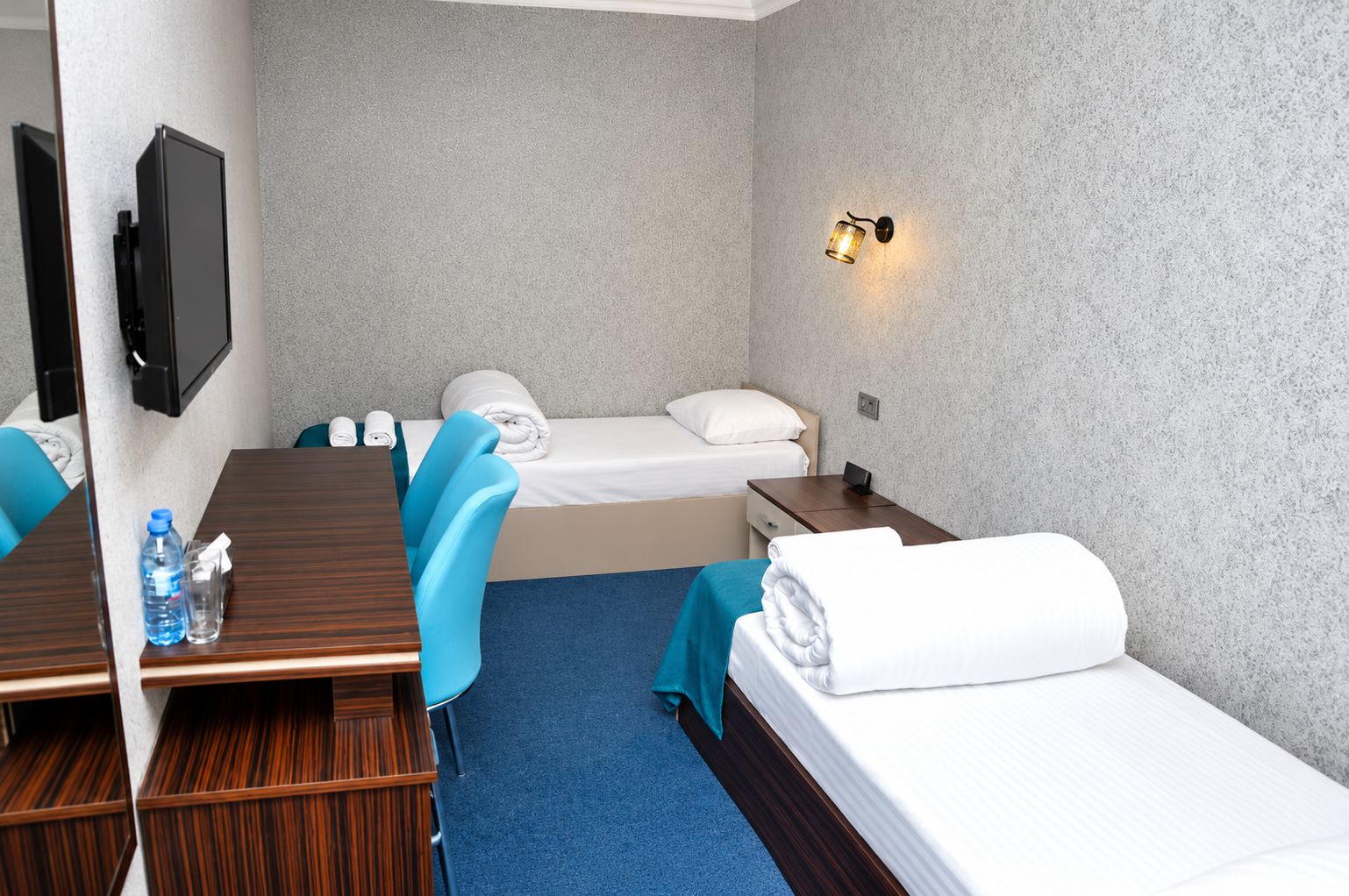Une chambre d’hôtel équipée d’un lit, d’un bureau, d’une chaise, d’une télévision et d’une lampe fixée au mur.