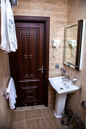 A bathroom with a wooden door, a white sink, a mirror, and a hairdryer. - Mildom Hotel Baku (Baku)