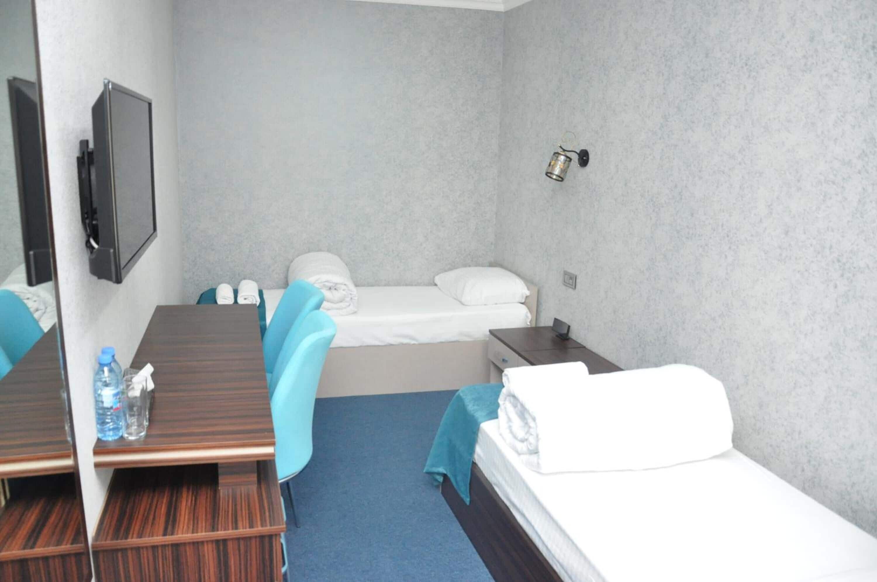 A hotel room with a wooden desk, blue chairs, a bed, and a small table.